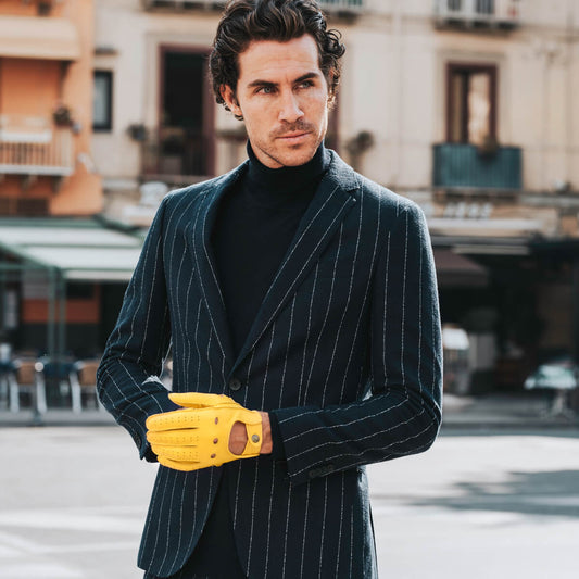 Man in a dark pinstripe suit with yellow gloves standing on a city street.