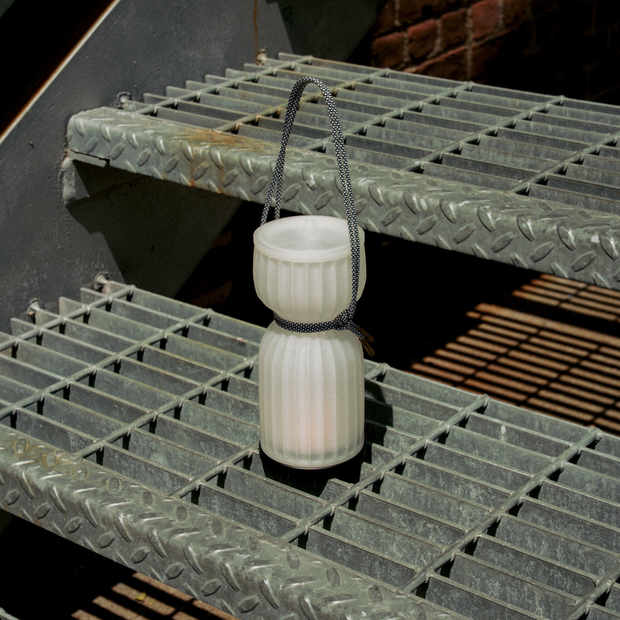 White lantern with a black cord on a metal grate
