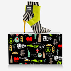 Zebra-striped high-heeled shoe with lime green accents on a BYMNYC branded box.