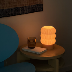 Small table with a textured lamp, glass, and book in a dimly lit room.