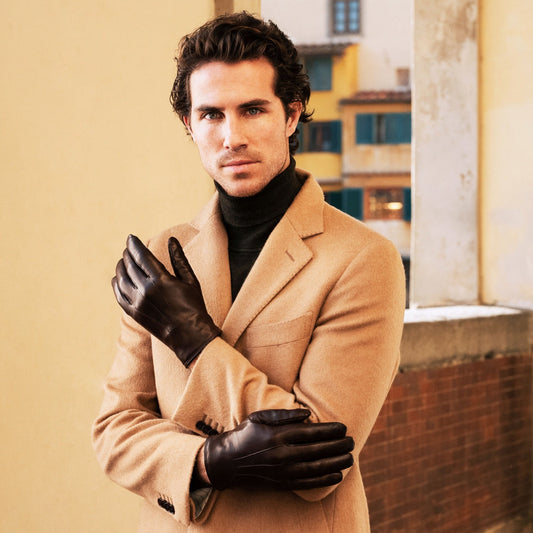 Man wearing a beige coat and black gloves standing in an urban setting.