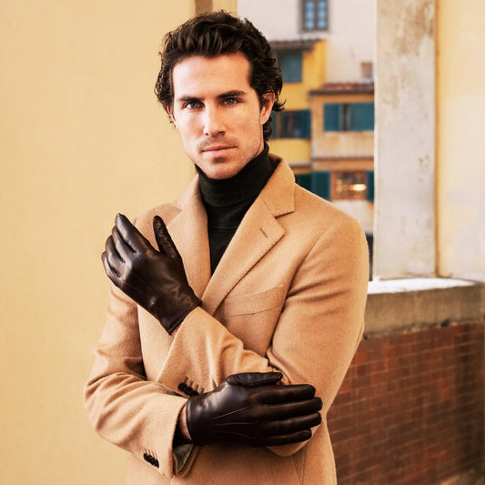 Man wearing a beige coat and black gloves standing in an urban setting.