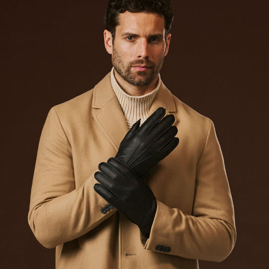 Man wearing a beige coat and black gloves against a brown background