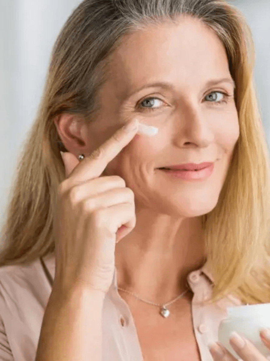 Woman applying cream to her face with a neutral background