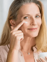 Woman applying cream to her face with a neutral background