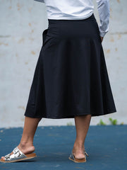 Person wearing a black skirt with a white shirt and sandals on a blue surface.