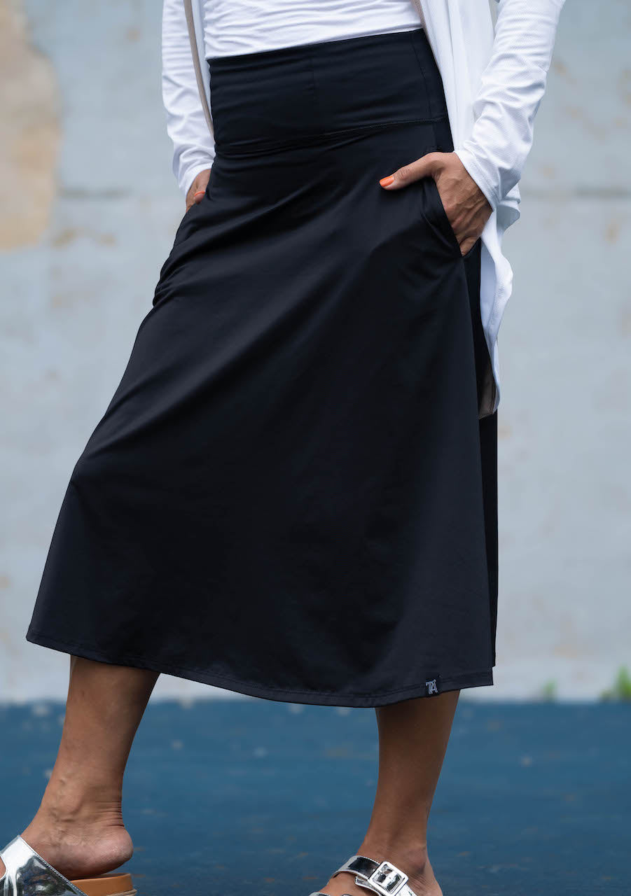 Person wearing a black skirt with a white shirt against a gray wall.