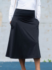 Person wearing a black skirt with a white top against a light gray wall.