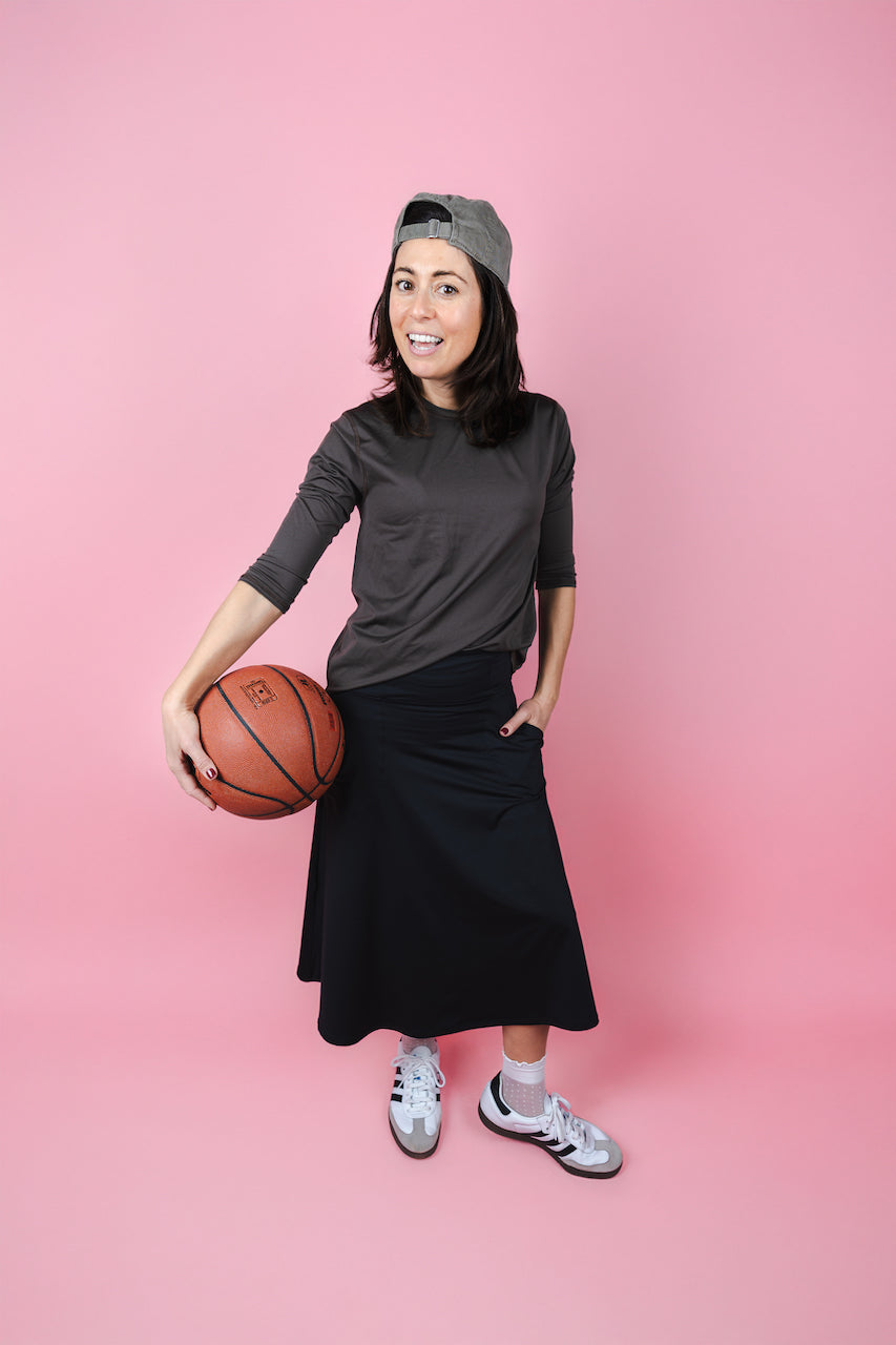 Person holding a basketball wearing a black outfit and gray cap on a pink background