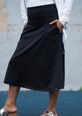 Person wearing a black skirt with a white shirt against a gray wall.