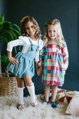 Two young girls in dresses standing on a textured surface with a dark background