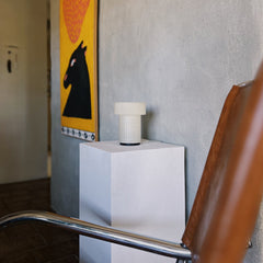 White cylindrical object on a stand with a horse painting in the background