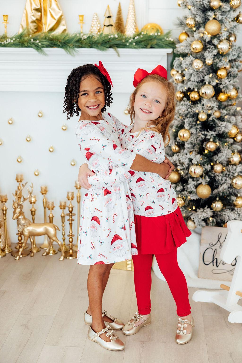 Two children in matching outfits standing in front of a decorated Christmas tree.
