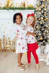 Two children in matching outfits standing in front of a decorated Christmas tree.