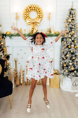 Child in a festive dress jumping in front of a decorated Christmas fireplace and tree.
