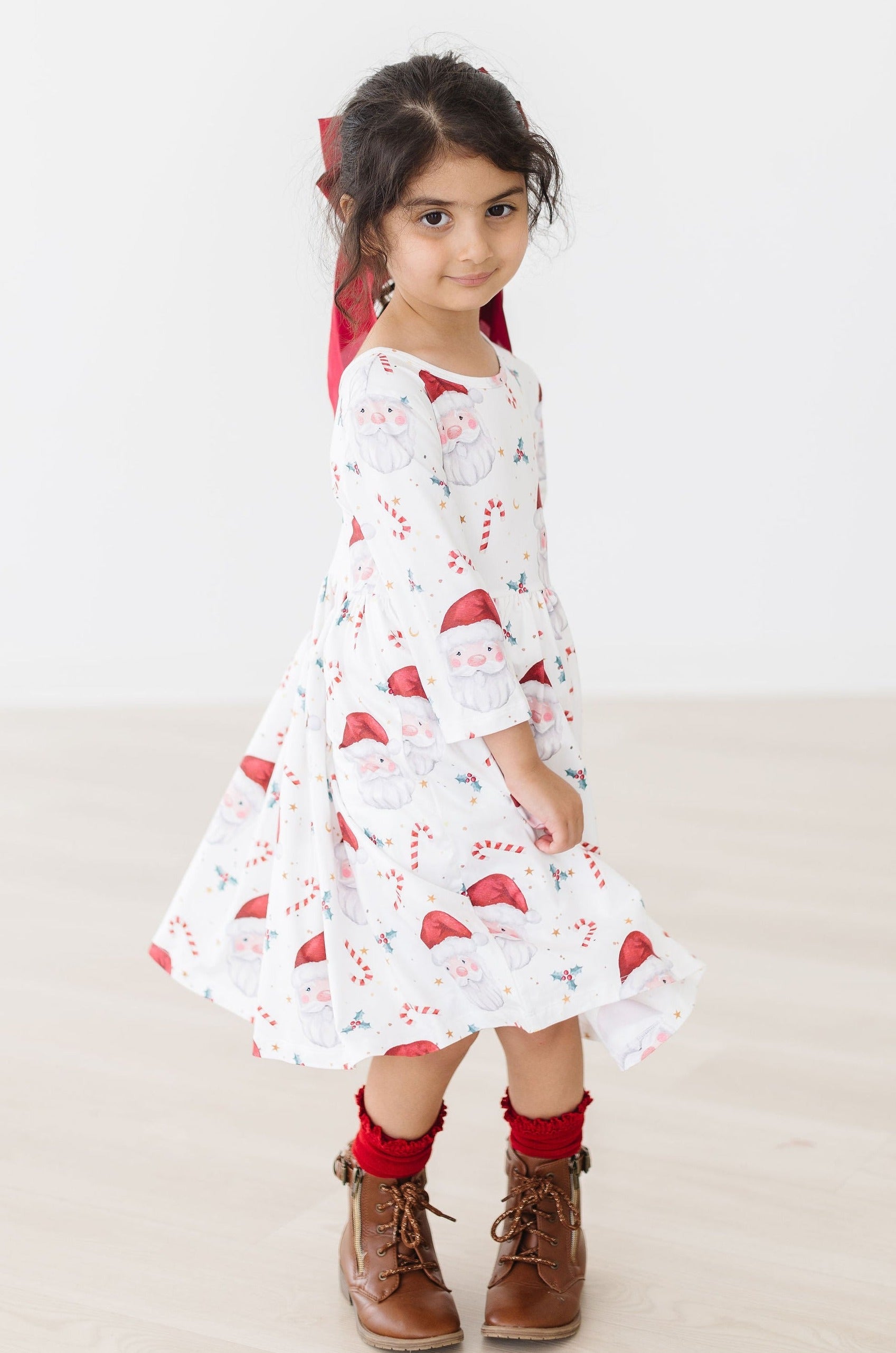 Young girl wearing a white dress with red patterns and brown boots on a light background