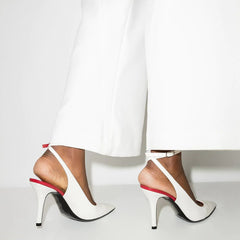 White high-heeled shoes with red accents worn by a person in white pants on a light gray background
