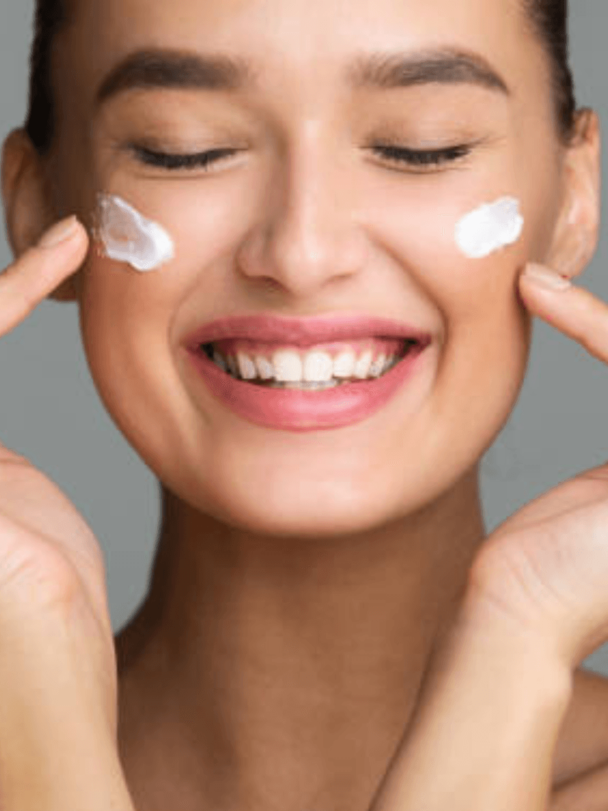 Woman applying cream to her face with a gray background