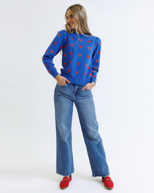 Woman wearing a blue sweater with red heart patterns and blue jeans on a white background