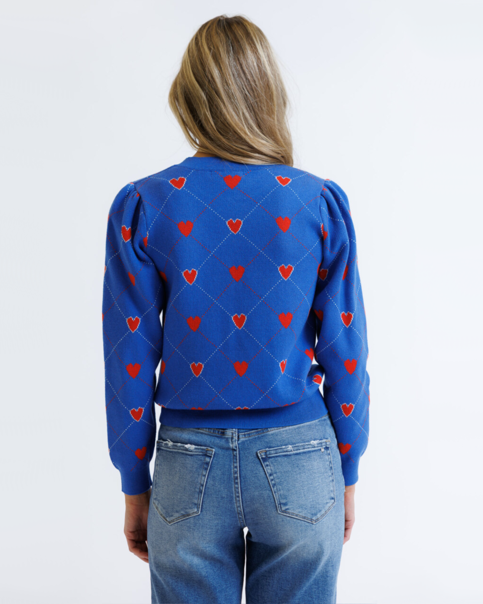 Person wearing a blue sweater with red heart patterns on a white background