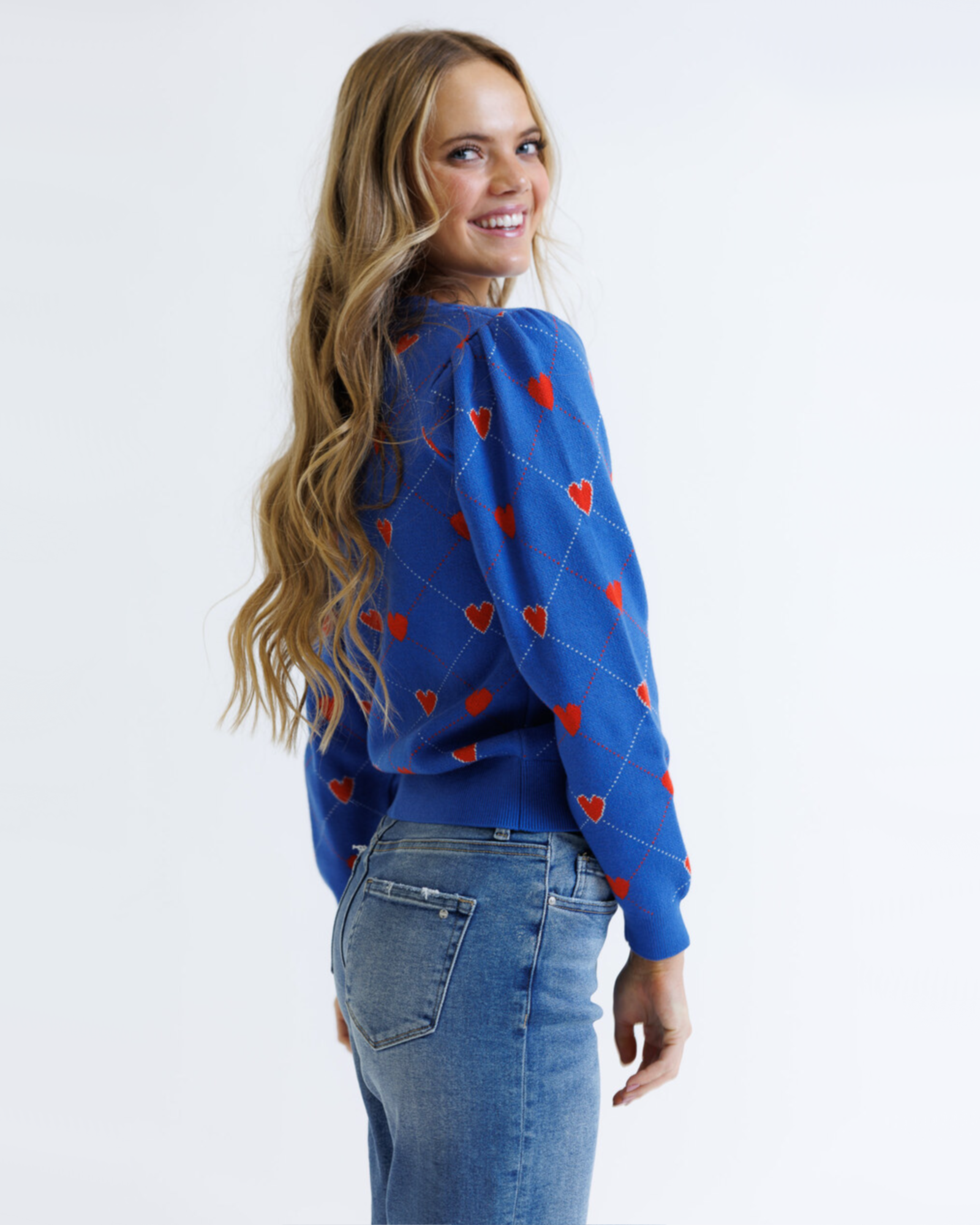 Woman wearing a blue sweater with red heart patterns and jeans on a white background