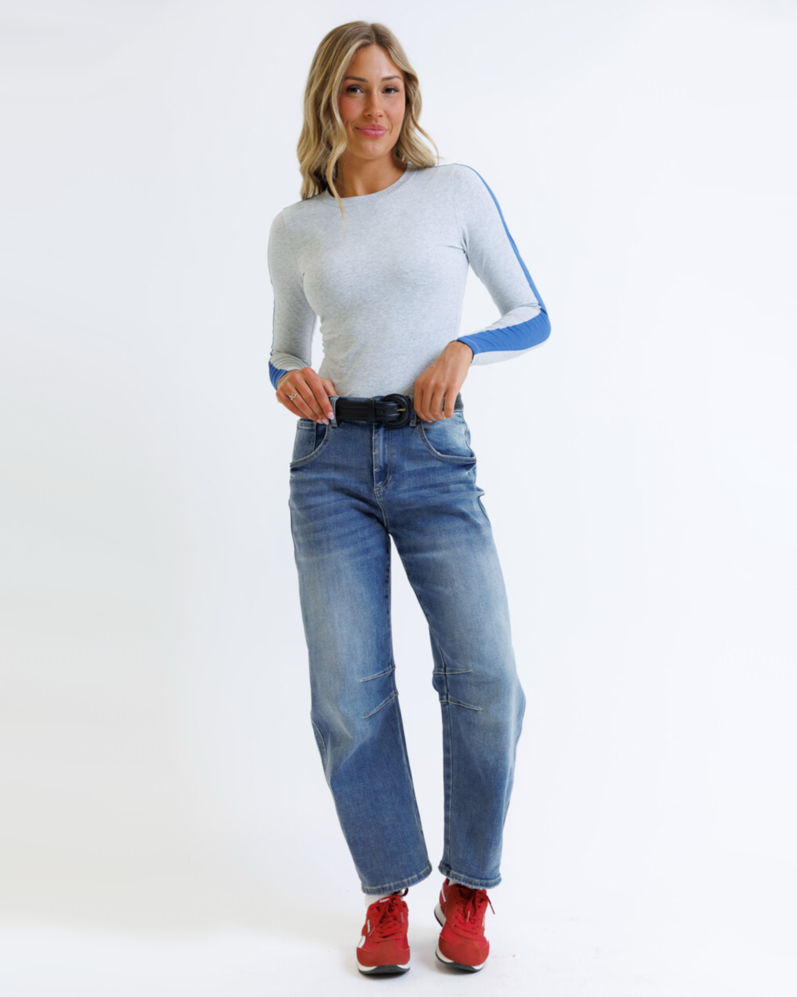 Woman wearing a light gray sweater with blue accents and blue jeans on a white background