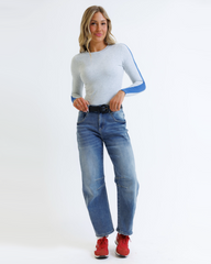 Woman wearing a light gray sweater with blue accents and blue jeans on a white background