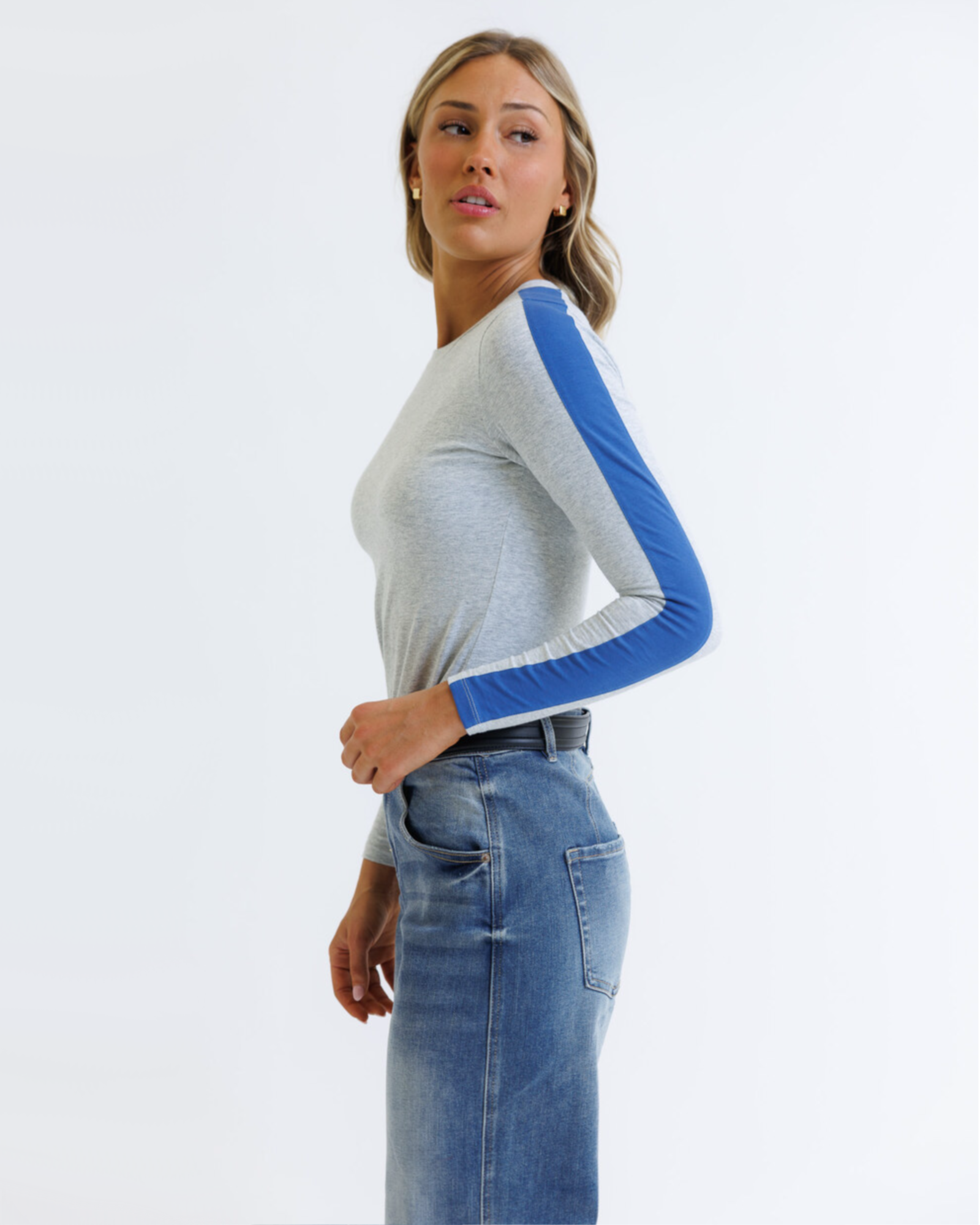 Woman wearing a gray and blue long-sleeve top with jeans on a white background