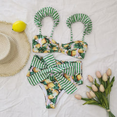 Bikini set with lemon and striped pattern on a white surface with a hat and flowers.