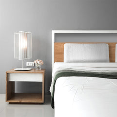 Modern bedroom with a bed, nightstand, and lamp against a gray wall.
