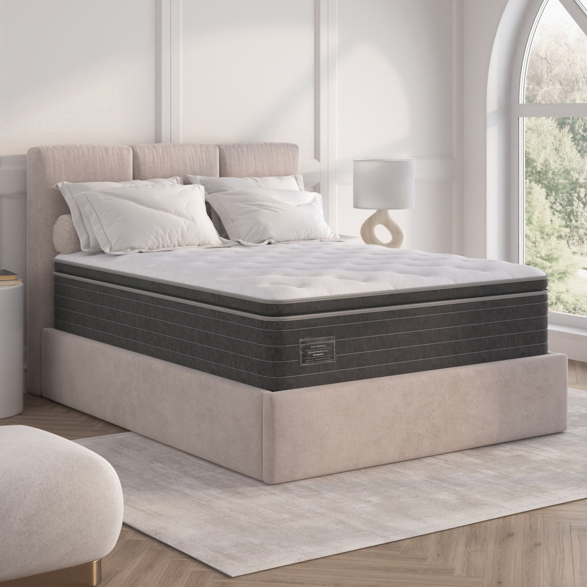 Gray mattress on a bed in a bedroom setting with a lamp and window in the background.