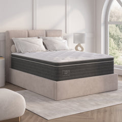Gray mattress on a bed in a bedroom setting with a lamp and window in the background.
