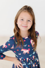 Young girl wearing a navy dress with colorful unicorn patterns on a white background