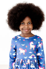 Young girl wearing a blue dress with unicorn pattern on a white background