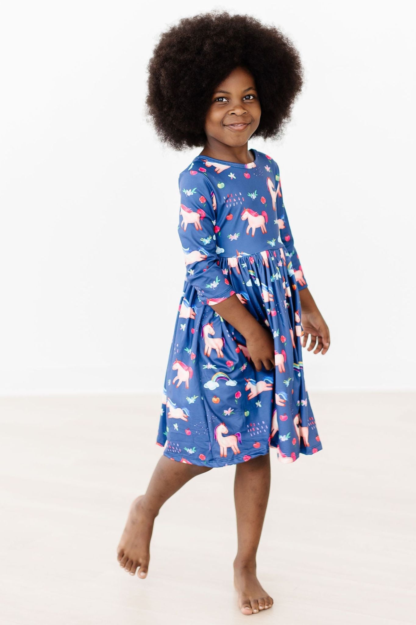 Child wearing a blue dress with unicorn pattern on a white background