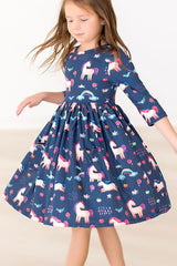 A young girl wearing a navy blue dress with a playful unicorn print, captured in motion against a bright, clean studio background.