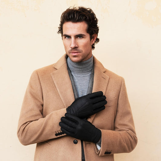 Man wearing a beige coat and black gloves against a beige background