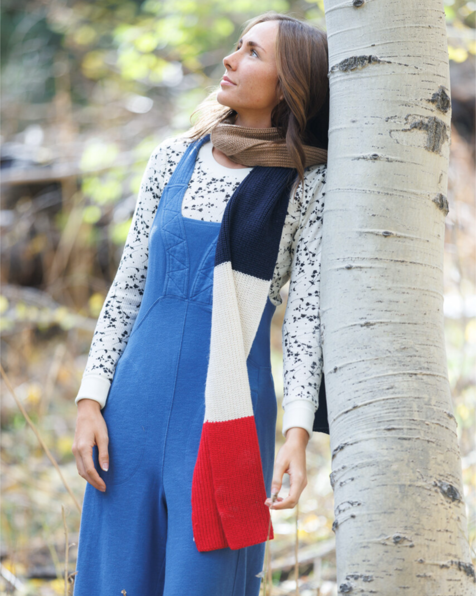 Woman in a colorful dress leaning against a tree in a natural setting