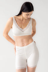 Woman wearing a white lace bralette and high-waisted shorts on a plain background