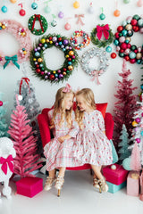 Two children sitting on a red chair surrounded by festive decorations including wreaths and Christmas trees.