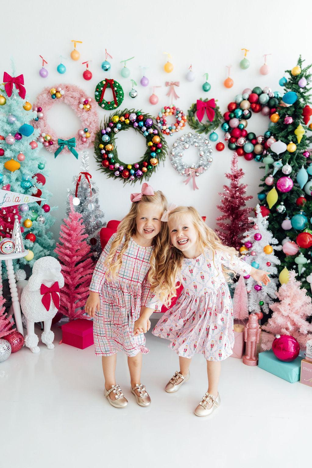 Two children posing in front of a festive Christmas backdrop with wreaths and decorations.