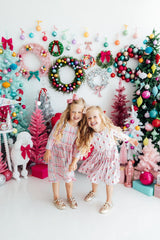 Two children posing in front of a festive Christmas backdrop with wreaths and decorations.