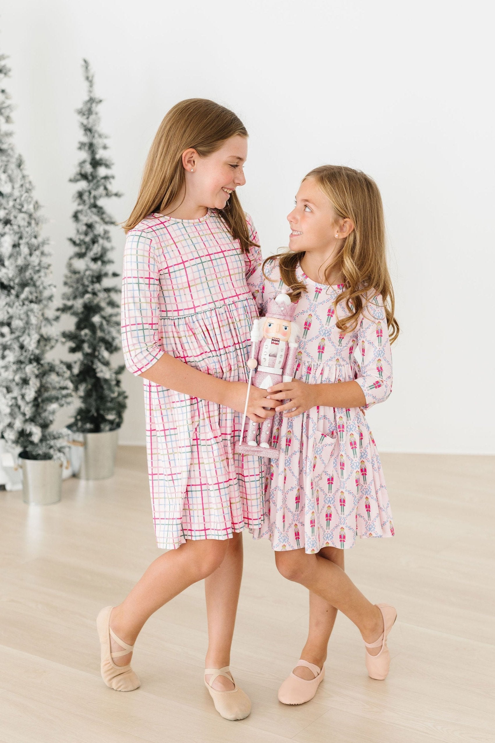 Two young girls in matching dresses standing in a room with a Christmas tree in the background.