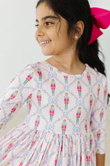 Young girl wearing a patterned dress with a pink bow in her hair against a white background