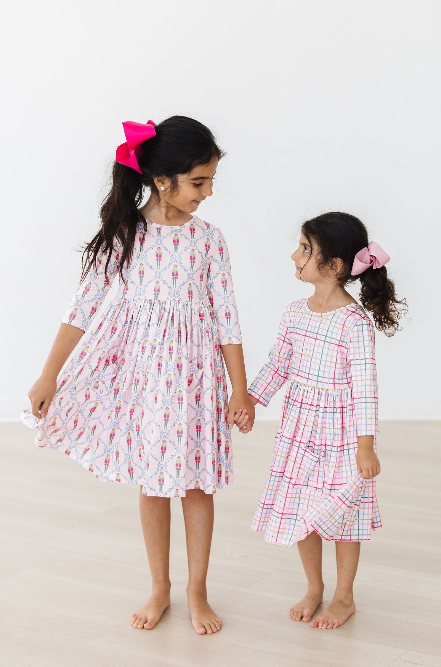 Two young girls wearing patterned dresses standing on a light background