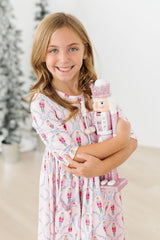Young girl holding a Nutcracker toy in a decorated room with Christmas trees.