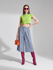 Woman wearing a green top, blue checkered pants, and pink boots on a gray background