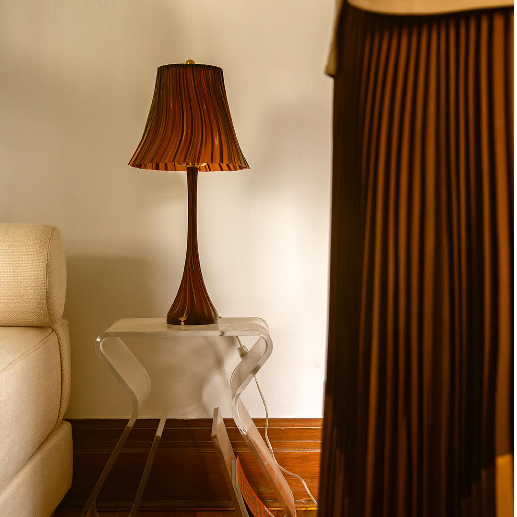 Table lamp on a side table next to a sofa with a curtain partially covering the view.