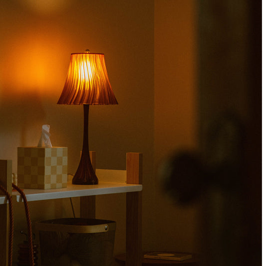 Table lamp with pleated shade on a wooden table in a dimly lit room.