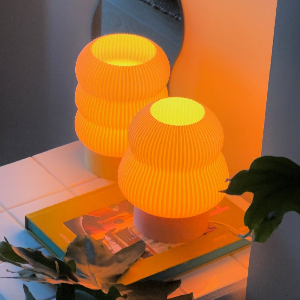 Two orange textured lamps on a surface with a book and plant